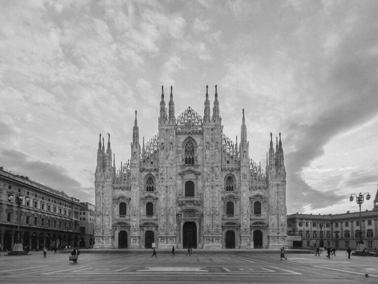 Cattedrale di Milano in bianco e nero, vista frontale con piazza e persone, architettura gotica con guglie elaborate.