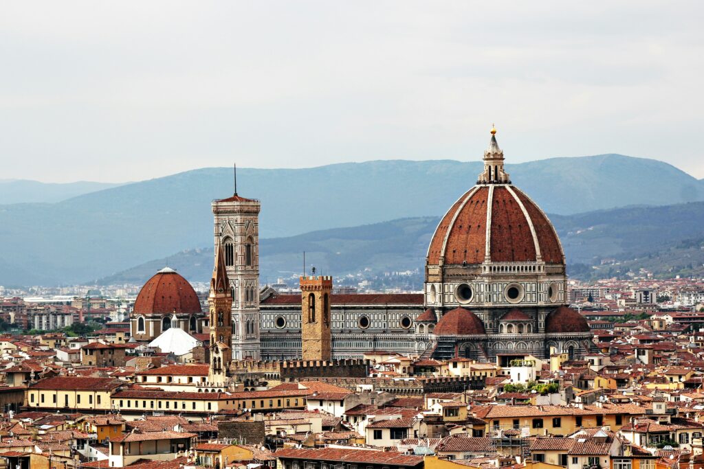 Cattedrale di Santa Maria del Fiore a Firenze con cupola brunelleschi e campanile di Giotto, circonda da edifici storici e montagne sullo sfondo