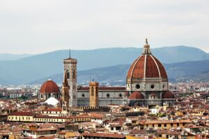 Cattedrale di Santa Maria del Fiore a Firenze con cupola brunelleschi e campanile di Giotto, circonda da edifici storici e montagne sullo sfondo