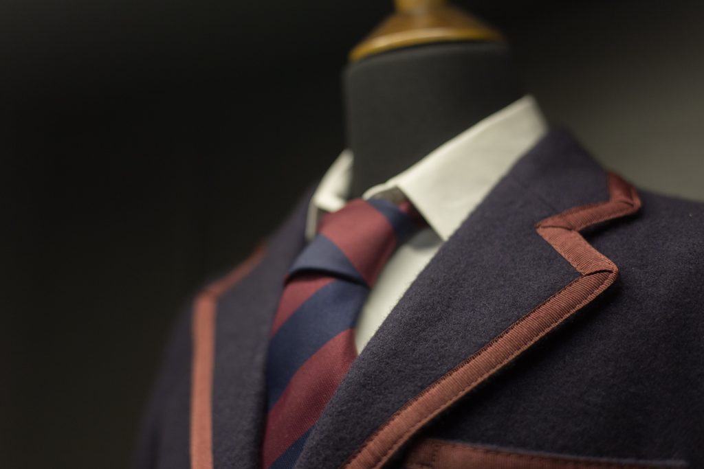 Manichino indossa blazer blu scuro con cravatta bordeaux e blu, colletto bianco e tasca color marrone.