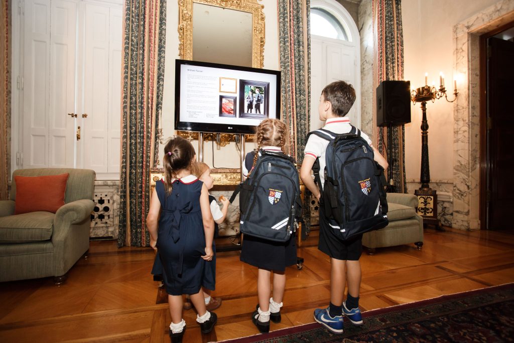 Three children in LM School Uniforms standing together, looking at a screen, representing the authenticity and craftsmanship of school uniforms used on film and television sets.