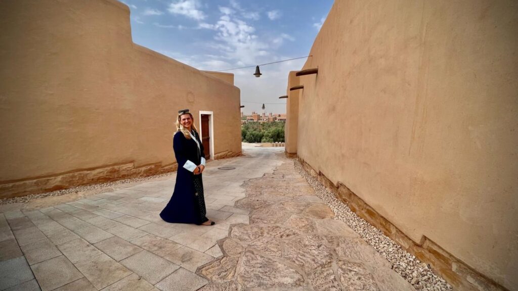 Donna in abito tradizionale in un cortile di adobe, architettura nord-africana con palme sullo sfondo