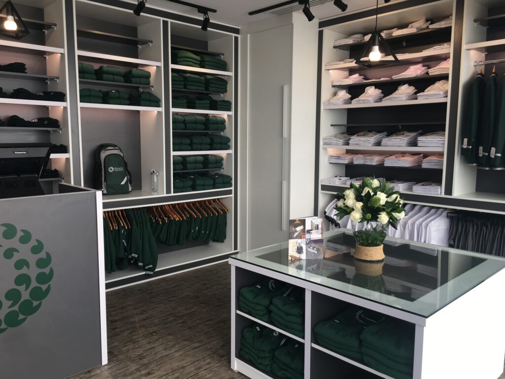 Showroom con scaffali di abbigliamento verde e bianco, banco vendita in vetro, fiori freschi e illuminazione moderna