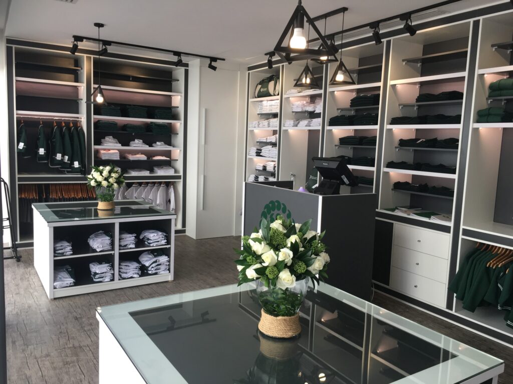 Boutique moderna con scaffali illuminati, capi appesi, pile di abbigliamento bianco e nero, tavoli espositivi e fiori decorativi.