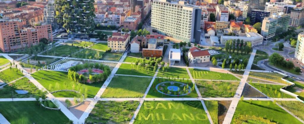 Urban park with geometric pathways, trees, and open green spaces surrounded by modern city buildings.