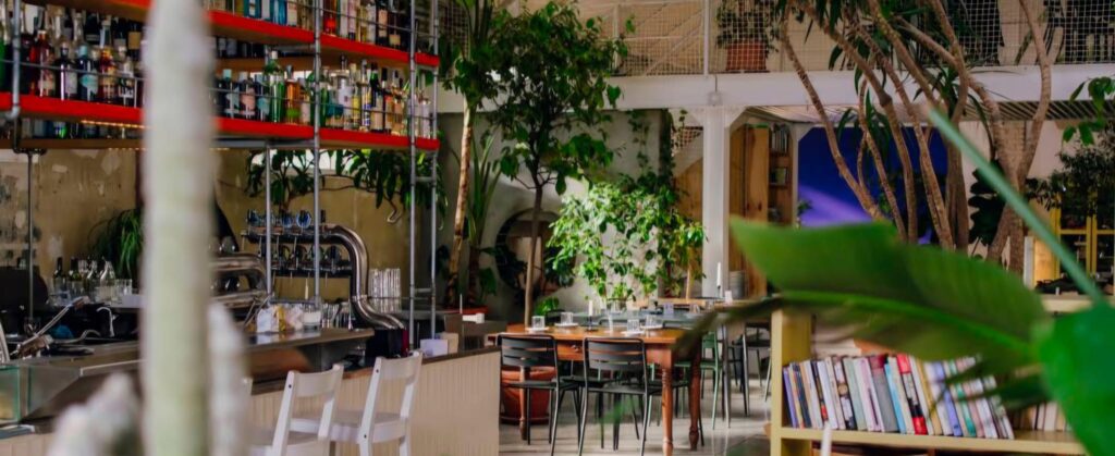 Large industrial-style coworking café in Milan, a flexible choice for where to study in Milan with open seating, plants, and group study areas.