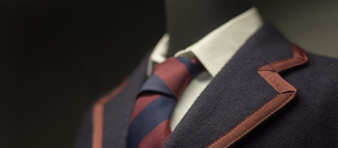 Manichino indossa blazer blu scuro con cravatta bordeaux e blu, colletto bianco e tasca color marrone.