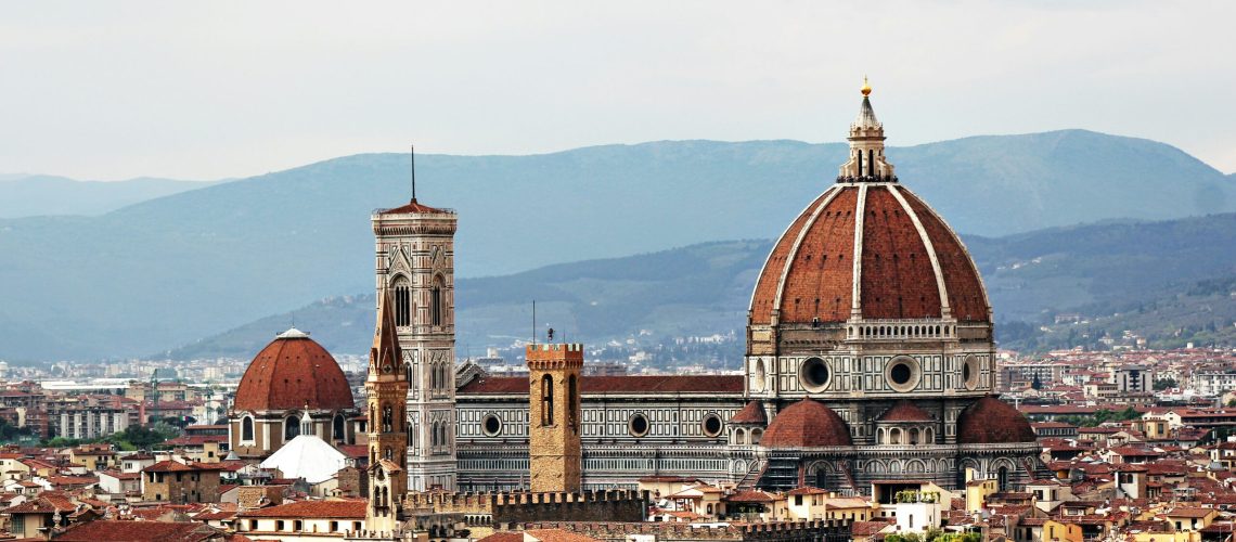 Cattedrale di Santa Maria del Fiore a Firenze con cupola brunelleschi e campanile di Giotto, circonda da edifici storici e montagne sullo sfondo